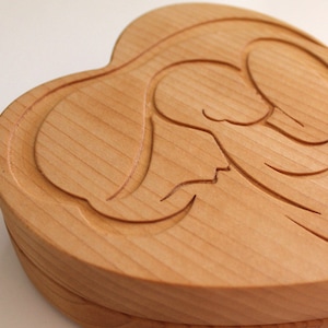 Peut inclure: Une bo&icirc;te en bois en forme de c&oelig;ur avec un motif d'ange sculpt&eacute; sur le couvercle. La bo&icirc;te est en bois de couleur claire, avec le grain du bois visible. Le motif de l'ange est sculpt&eacute; en relief, ajoutant de la profondeur et de la texture.