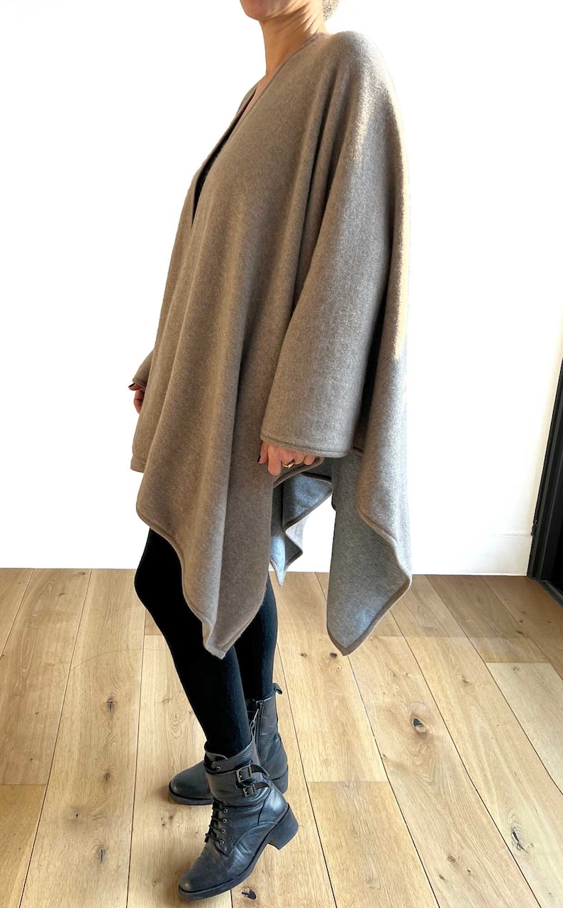 May include: A brown knitted poncho with a long, asymmetrical hemline. The poncho is worn over black leggings and black boots.