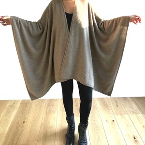 May include: A brown cashmere wrap with a long, flowing design. The wrap is draped over a person wearing black leggings and black boots.