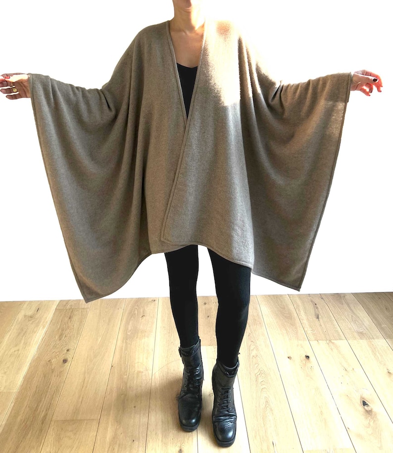 May include: A brown cashmere wrap with a long, flowing design. The wrap is draped over a person wearing black leggings and black boots.