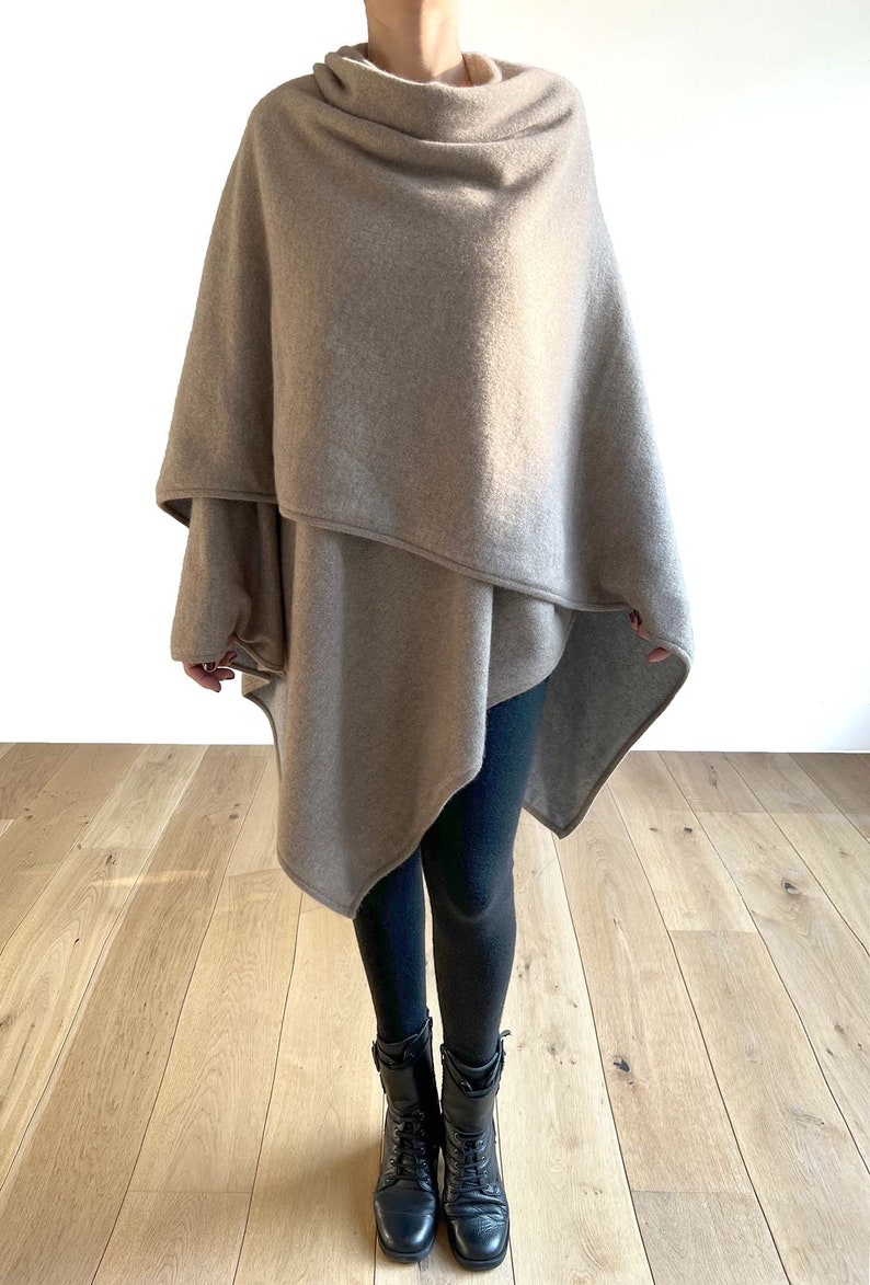 May include: A beige cashmere wrap with a draped design. The wrap is worn over black leggings and black boots.