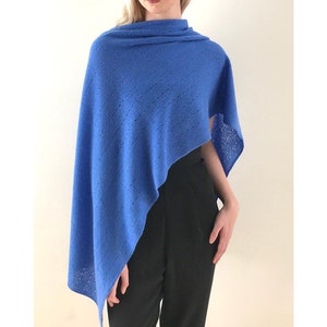 May include: A blue knitted poncho with a delicate openwork pattern. The poncho is draped over a person's shoulders and is styled with black pants.