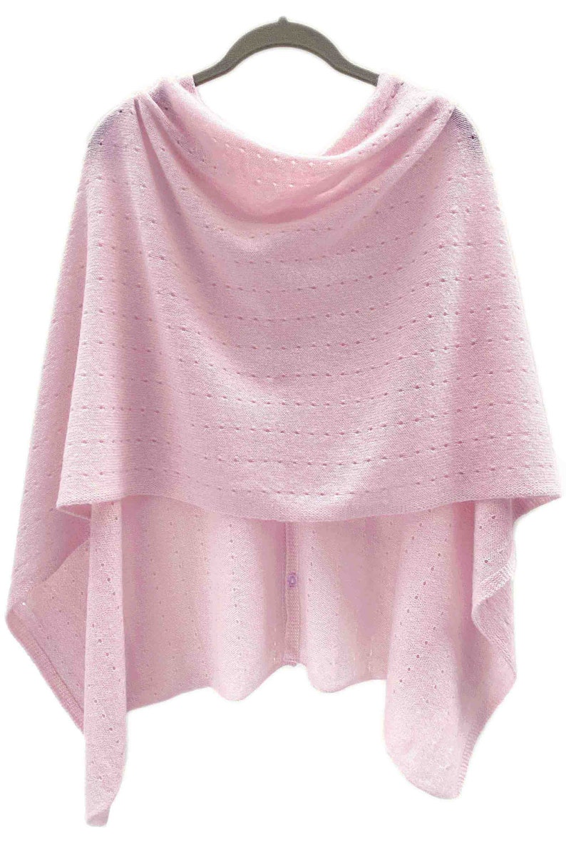 May include: A pink knitted poncho with a button closure. The poncho has a delicate openwork pattern.