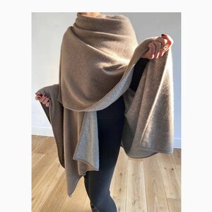May include: A brown and gray cashmere wrap with a reversible design. The wrap is draped over a person's shoulders and is worn with black pants.