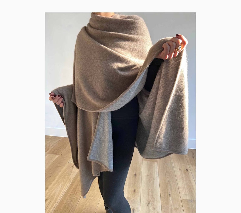 May include: A brown and gray cashmere wrap with a reversible design. The wrap is draped over a person's shoulders and is worn with black pants.