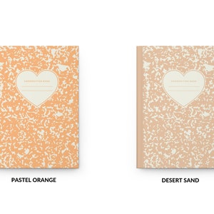 May include: Two composition notebooks with a heart-shaped design on the front cover. The notebook on the left is pastel orange and the notebook on the right is desert sand.