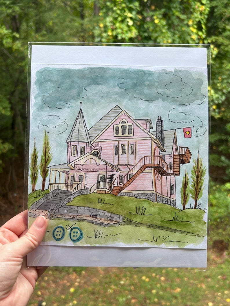 May include: Watercolor painting of a pink Victorian house on a green hill, with a wooden staircase and a small flag. The artwork is held in a clear plastic sleeve, with two blue buttons at the bottom.