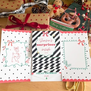 Può includere: Porta carte regalo a tema natalizio con un design a pois rosa e bianchi. Una carta presenta una renna, un'altra ha uno spazio vuoto e la carta centrale recita "Season's surprises inside". Sono visibili anche una confezione regalo e delle forbici.