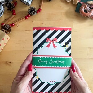 May include: A Christmas card with a black and white striped background, a red scalloped border, and a green band that reads "Merry Christmas." The card features a white decorative shape with a red bow and small yellow stars.
