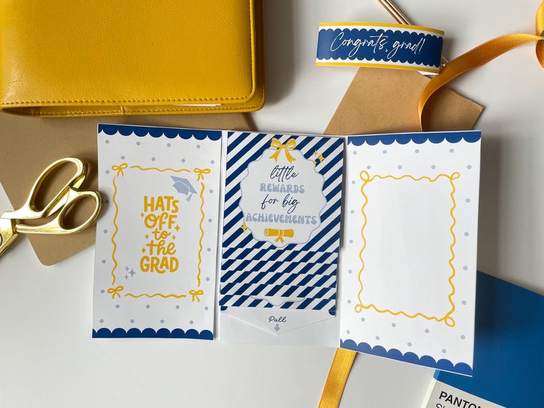 May include: A graduation card with a blue and white striped design, featuring the text "Hats Off to the Grad" and "Little Rewards for Big Achievements." A yellow wallet, scissors, and a ribbon are also visible.