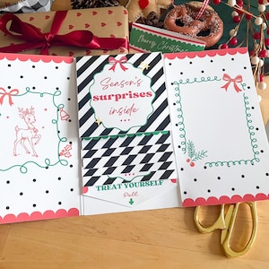May include: A festive Christmas card with a pink scalloped edge, black polka dots, and a reindeer illustration. The card reads "Season's surprises inside" and "Treat Yourself, Pull". A pair of gold scissors is on the wooden surface.