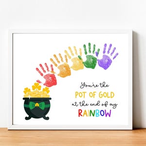 Puede incluir: Impresión enmarcada con una olla de oro negra y un arcoíris de huellas de manos rojas, naranjas, amarillas, verdes y moradas. El texto dice: "Eres la olla de oro al final de mi arcoíris". La olla tiene un lazo verde.