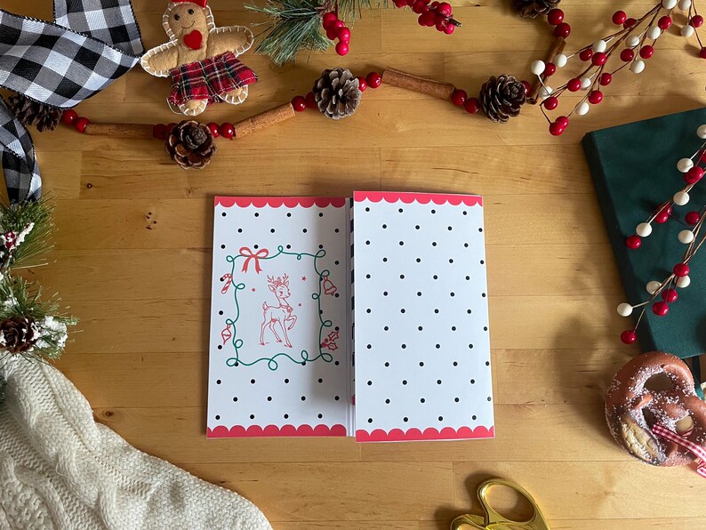 May include: Open Christmas card with a white background and black polka dots. The left side features a red and green illustrated reindeer design. The card has a scalloped pink border. Festive holiday decor surrounds the card.
