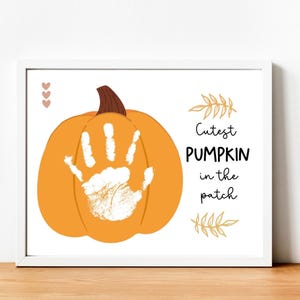 Pode incluir: Uma moldura branca com uma impressão de mão branca em uma abóbora laranja. O texto diz "Cutest PUMPKIN in the patch".