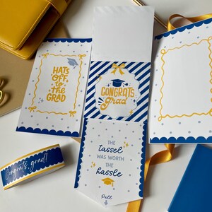 May include: A graduation stationery set in blue and yellow. The set includes cards with scalloped edges and text such as "Hats off to the Grad" and "Congrats Grad." A matching ribbon and a blue notebook are also visible.
