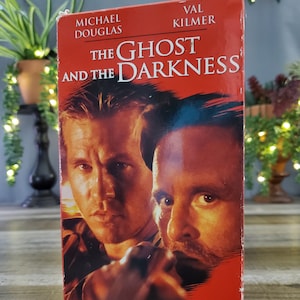 Puede incluir: Una cinta VHS de la película "The Ghost and the Darkness" con Michael Douglas y Val Kilmer. La portada es predominantemente roja con imágenes de los actores. También se ve el texto "Prey for the Hunters".