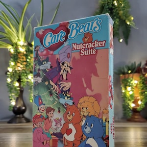 May include: A vintage VHS tape of the Care Bears Nutcracker Suite. The box features colorful illustrations of Care Bears, villains, and children. The title is in red and white, with a blue background. The tape is a full-color animated feature presentation.