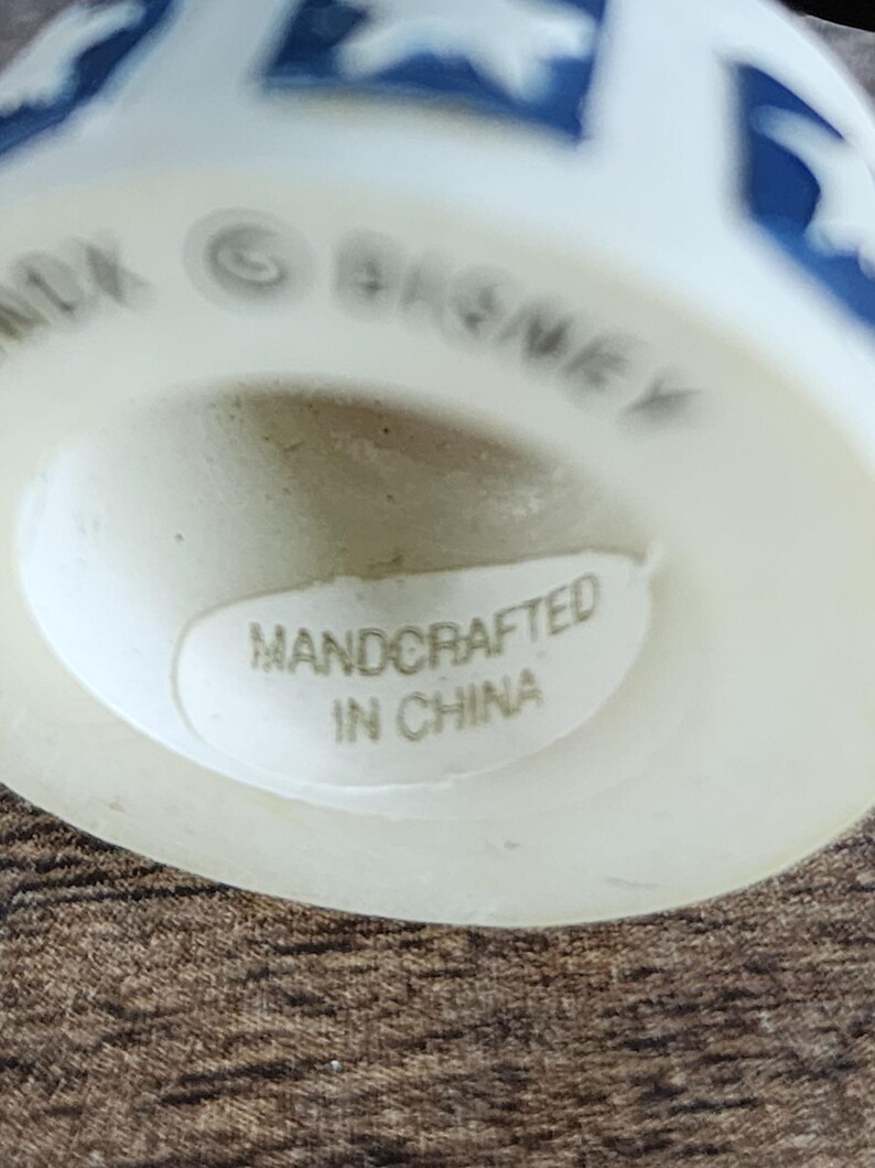 May include: A white ceramic figurine with blue star-shaped designs. The base of the figurine has the text "HANDCRAFTED IN CHINA" on a sticker. The word "DISNEY" is also visible.