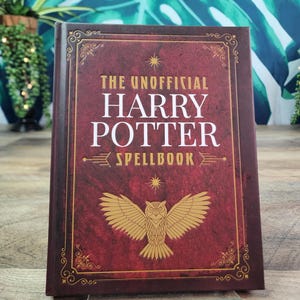 May include: A hardcover book titled The Unofficial Harry Potter Spellbook with a deep red textured cover, gold filigree border, and a central gold owl illustration. The text is printed in white and gold lettering on the front cover.