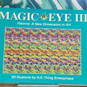 May include: A teal book titled "MAGIC EYE III" with the subtitle "Visions: A New Dimension in Art." The cover features a colorful 3D illusion pattern. The text "3D Illusions by N.E. Thing Enterprises" is at the bottom.