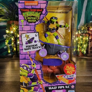 May include: A Teenage Mutant Ninja Turtles Mutant Mayhem Half Pipe RC Donnie toy in its original packaging. The box features a purple brick wall design, a graphic of Donnie, and a clear window displaying the green action figure on a skateboard.