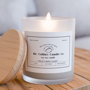 Puede incluir: Un tarro de vela de vidrio esmerilado con una tapa de madera. La vela está encendida y la etiqueta dice "Mr. Collins Candle Co. vela de cera de soja "what on exemplary vegetable" 11 oz 50 horas".