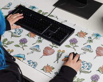 May include: A white desk mat with a floral pattern featuring mushrooms, flowers, and leaves. A person is using a black keyboard and a computer mouse on the mat.