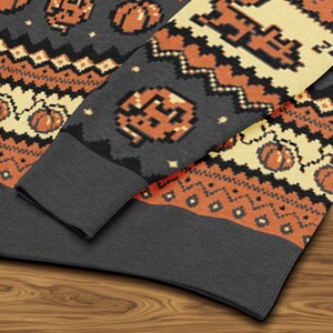 Puede incluir: Primer plano de un su&eacute;ter gris de Halloween con calabazas pixeladas de color naranja y crema y patrones geom&eacute;tricos. El su&eacute;ter tiene un pu&ntilde;o gris acanalado y cuello redondo. El dise&ntilde;o recuerda a los gr&aacute;ficos de videojuegos retro.