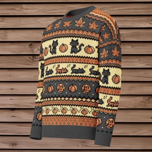 Puede incluir: Un su&eacute;ter de Halloween gris, naranja y crema con gatos negros pixelados, calabazas y hojas de oto&ntilde;o. El su&eacute;ter tiene cuello, pu&ntilde;os y dobladillo de canal&eacute;. El dise&ntilde;o se repite en la parte delantera y las mangas.