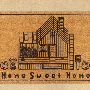 May include: A rectangular doormat with a house illustration and the words "Home Sweet Home" in black. The house design includes a chimney, windows, and a door. Two small animal figures are on the left side of the mat.