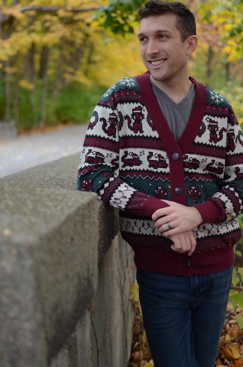 May include: A burgundy and cream-colored cardigan sweater with a repeating pattern of cartoon animals and snowflakes. The sweater has a V-neck and button closure. The person is wearing a gray t-shirt and blue jeans.