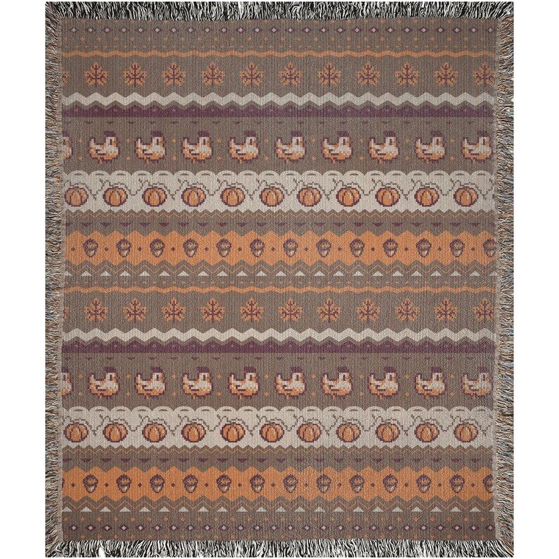 May include: A rectangular throw blanket with a repeating pattern of pumpkins, acorns, leaves, and birds in shades of brown, orange, and purple. The blanket has a fringed edge.