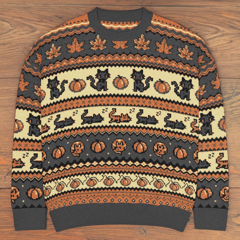 Puede incluir: Jersey gris de cuello redondo con un patr&oacute;n repetido de gatos negros, calabazas y hojas de arce en naranja y crema. El jersey tiene cuello, pu&ntilde;os y dobladillo de canal&eacute;. Una prenda festiva con tem&aacute;tica de oto&ntilde;o o Halloween.