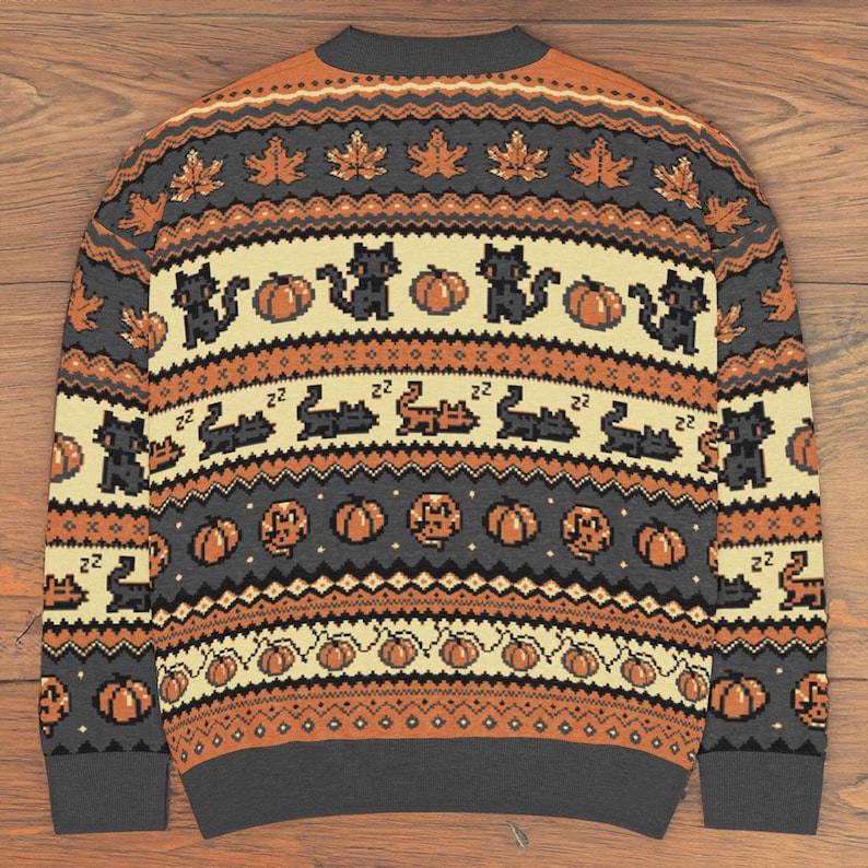 Puede incluir: Un su&eacute;ter de Halloween gris, naranja y crema con un patr&oacute;n repetido de gatos negros, calabazas y hojas de arce. El su&eacute;ter tiene cuello redondo y mangas largas, perfecto para la temporada de oto&ntilde;o.