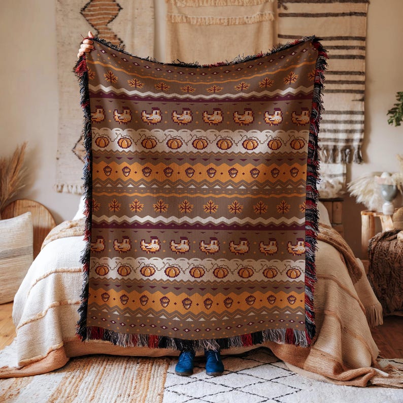 May include: A brown throw blanket with a repeating pattern of pumpkins, acorns, and birds. The blanket has a fringed edge with red and black accents. The design is in shades of brown, orange, and white, perfect for fall decor.