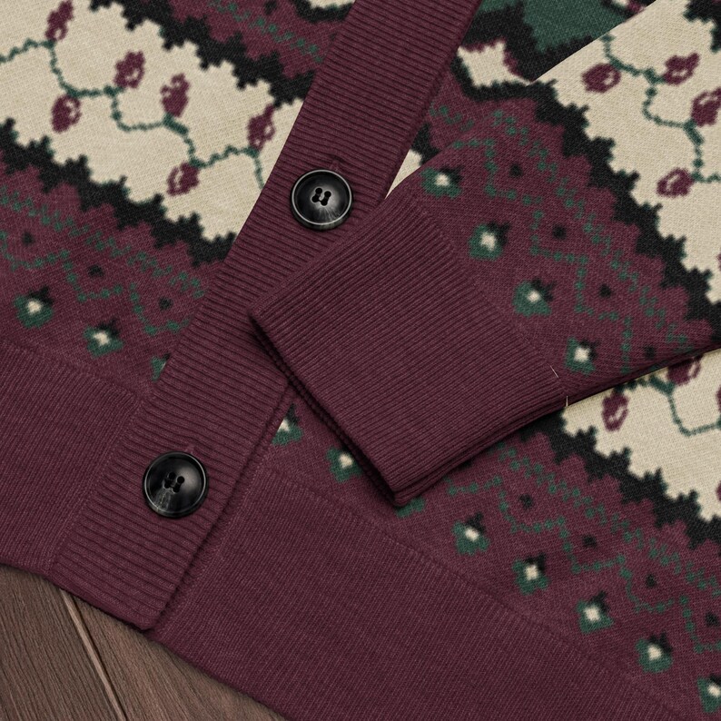 May include: A burgundy cardigan sweater with a patterned design in cream, green, and black. The sweater has a ribbed cuff and hem, and two black buttons. The pattern includes floral and geometric shapes.