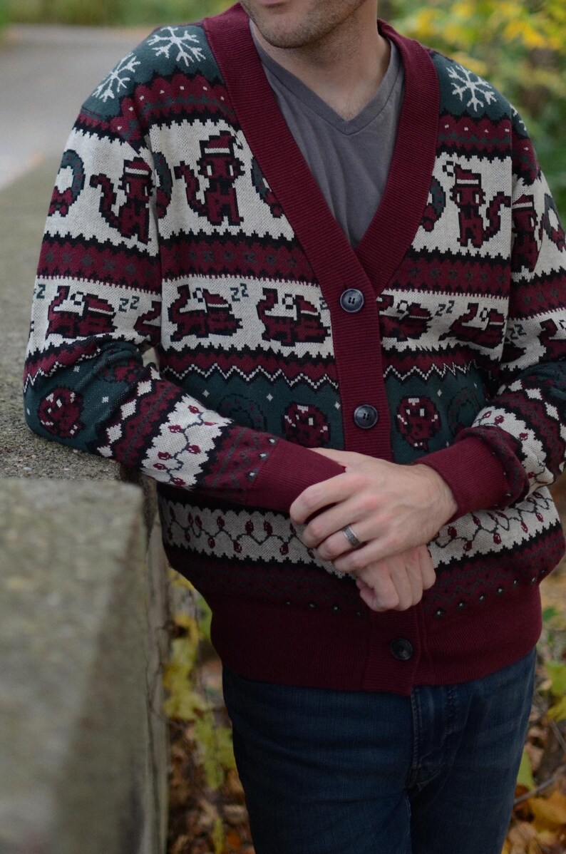 May include: Burgundy and green Christmas-themed cardigan sweater with a button-up front. The sweater features a pattern of pixelated animals, snowflakes, and other holiday designs. The cuffs and trim are a solid burgundy color.