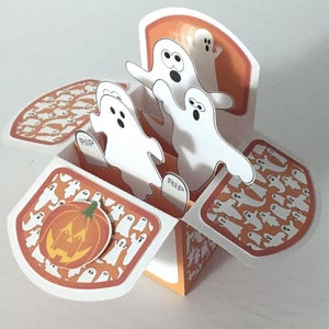 May include: A pop-up card with a Halloween theme. The card features a pumpkin and three ghosts with the word "RIP" on the tombstones. The background is orange with a pattern of white ghosts.