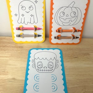 May include: Three Halloween-themed coloring cards with black and white line drawings of a ghost, a pumpkin, and a Frankenstein monster. Each card has two slots for crayons, and two crayons are included.