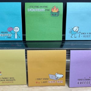 May include: A collection of six square sticky notes in various colors. Each note features a humorous illustration and text. The notes include phrases like "Hey, you dropped this," and "Back & Body Hurts." The overall theme is office humor.