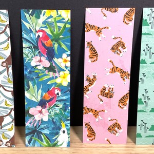 May include: Four colorful bookmarks with jungle animal designs. One features monkeys and bananas, another parrots and flowers, a third tigers, and the last crocodiles. The bookmarks are rectangular and stand upright.