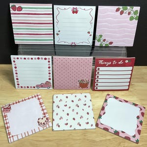 May include: A selection of square sticky notes featuring strawberry designs. Patterns include pink stripes, lined pages, polka dots, and strawberry illustrations. One note reads "Things to do."