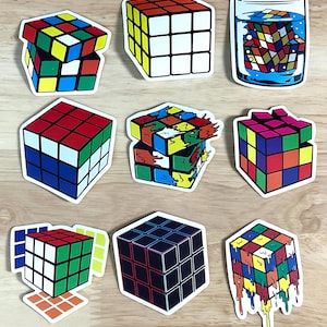 May include: Nine colourful Rubik's Cube stickers in different designs. The stickers show classic cube patterns, melting effects, and a cube in water. The cubes are in red, blue, yellow, green, and white.
