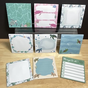 May include: A collection of eight square sticky note pads featuring sea turtle illustrations. Designs include water patterns, pink backgrounds with turtles, blue wave motifs, and a green list pad with the text Things to do at the top.