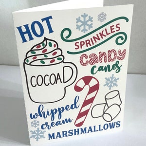 May include: A white card with a hand-drawn illustration of a cup of hot chocolate with whipped cream, sprinkles, candy canes, and marshmallows. The text on the card reads "HOT COCOA whipped cream MARSHMALLOWS sprinkles candy canes".