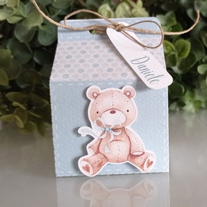 Può includere: Una scatola regalo azzurra con un motivo a pois bianchi e un'illustrazione di un orsacchiotto. La scatola ha un'etichetta che dice "Danielle".