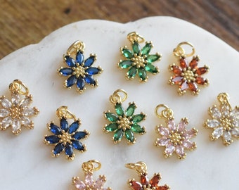 May include: Assortment of gold flower charms with various colored crystal accents. The charms are arranged on a white surface.