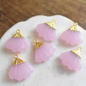 May include: Six pink glass flower charms with gold accents. The charms have a fan-like shape and are perfect for jewelry making.