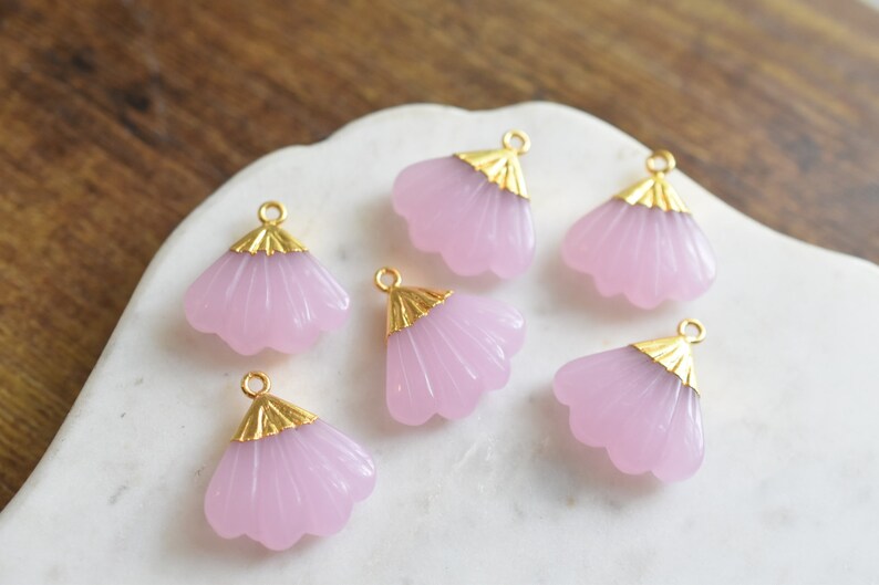 May include: Six pink glass flower charms with gold accents. The charms have a fan-like shape and are perfect for jewelry making.