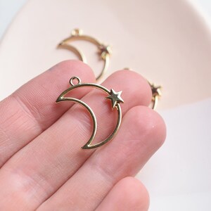 May include: Gold metal crescent moon charm with a small star in the center. The charm has a loop at the top for attaching to jewelry or other crafts.